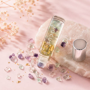 Crystal-infused Focus roller bottle with gold flakes in a soft pink minimalist flat lay setup