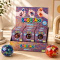 A display box of Gel Bead Multi Smooshos Balls with three individual packs in front, styled on a wooden surface with two colorful gel balls in the foreground and a plant in the background.