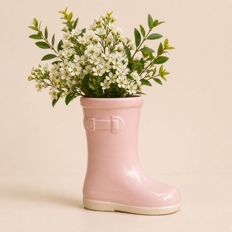 Pink rain boot with a bouquet of white flowers on a beige background