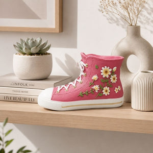 Pink floral gym boot resin vessel displayed on a modern wooden shelf with decorative books, succulent plant, and ceramic décor.