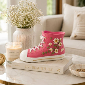 Pink gym boot resin vase filled with white daisies and greenery on a wooden tabletop with elegant floral accents.