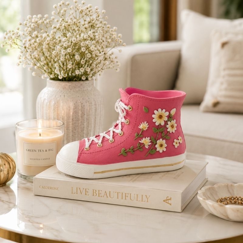Pink gym boot resin vase filled with white daisies and greenery on a wooden tabletop with elegant floral accents.