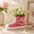 Pink floral sneaker planter filled with fresh daisies displayed on a sunlit cottage-style windowsill surrounded by flowers.