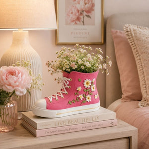 Pink sneaker-shaped floral resin planter styled on a bedside table with flowers, books, and soft bedroom décor.