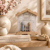 Family hanging plaque with pebble figurines styled on stacked books with blush florals and neutral home decor accessories.