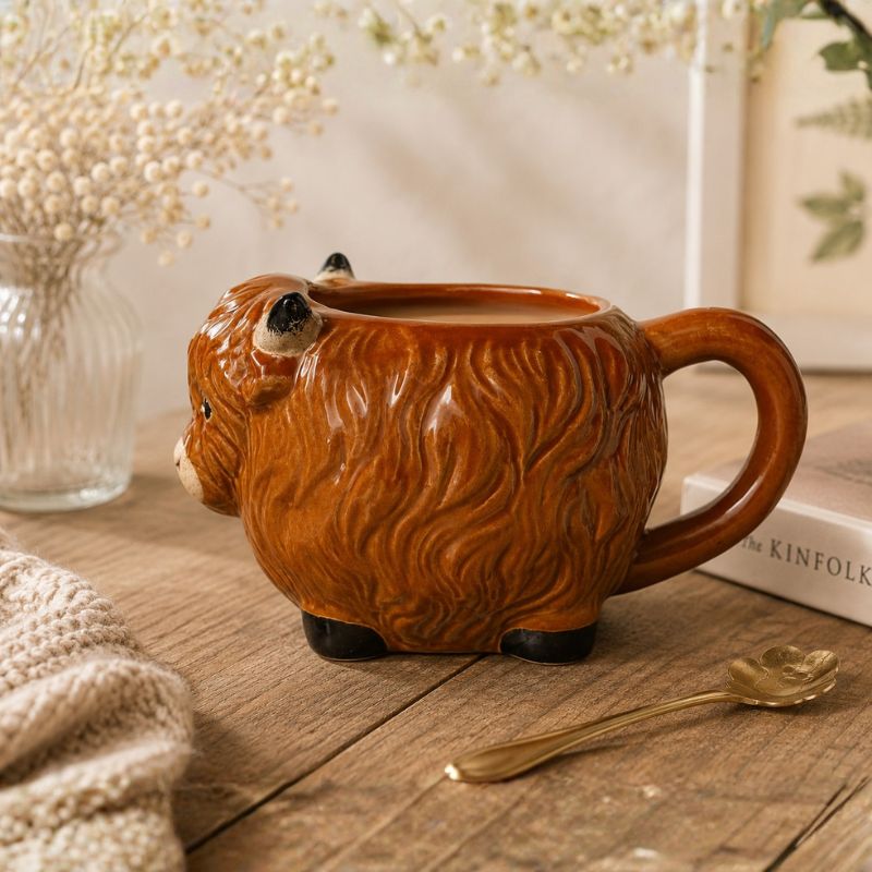 Highland Cow mug on a wooden surface with a spoon and books in the background.-Loveshack Giftware