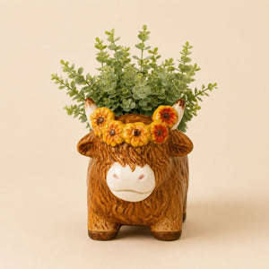 Ceramic cow planter with greenery on a beige background