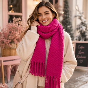A smiling woman wearing a Hot Pink Chunky Knit Winter Scarf and a cream-colored coat, standing in a softly blurred outdoor cafe setting.