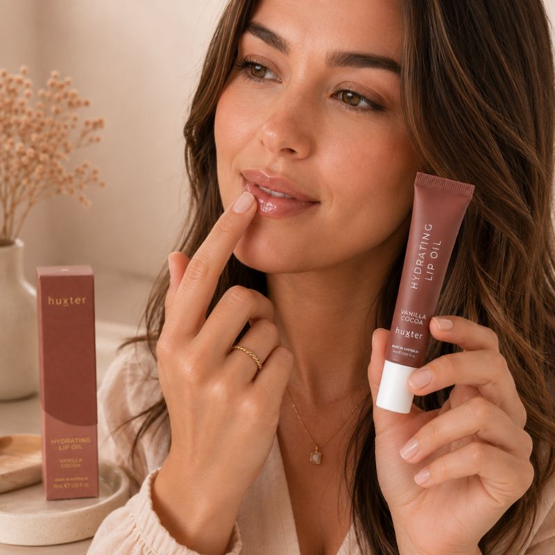 Woman applying Huxter Vanilla Cocoa Hydrating Lip Oil with fingertip in beauty lifestyle scene