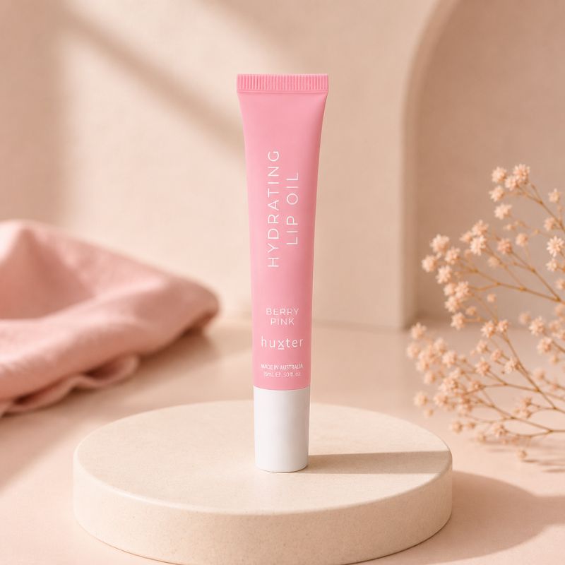 Huxter Berry Pink Hydrating Lip Oil tube displayed on cream pedestal in pink studio setting