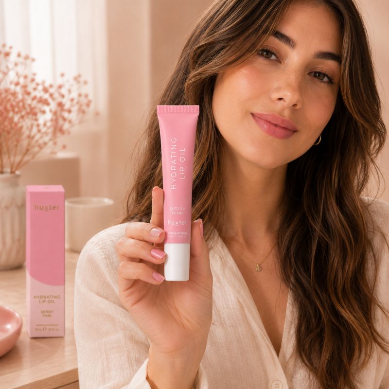 Woman holding Huxter Berry Pink Hydrating Lip Oil in a soft blush beauty setting