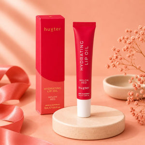 Huxter Melon Red Hydrating Lip Oil with matching box on coral blush studio background