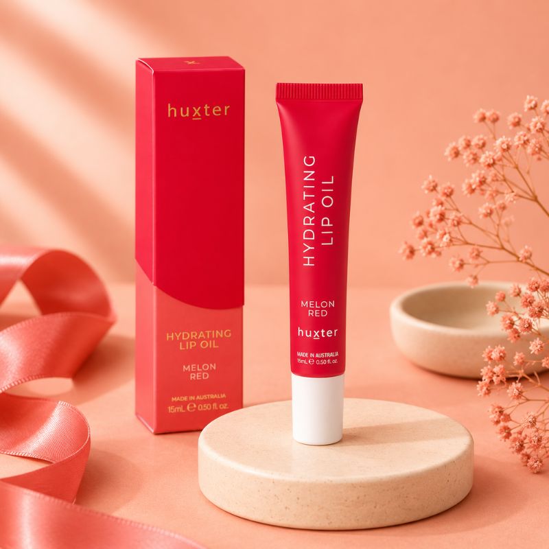 Huxter Melon Red Hydrating Lip Oil with matching box on coral blush studio background