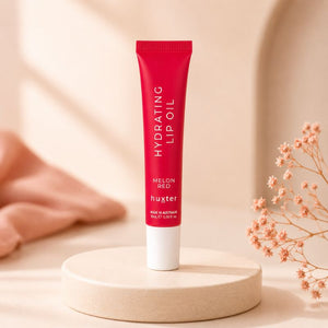 Huxter Melon Red Hydrating Lip Oil tube on cream pedestal with coral blush styling