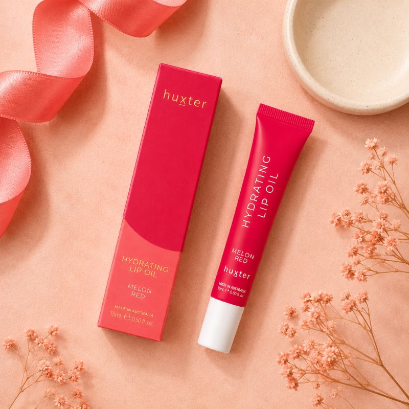 Huxter Melon Red Hydrating Lip Oil tube and matching box in overhead coral blush flat lay