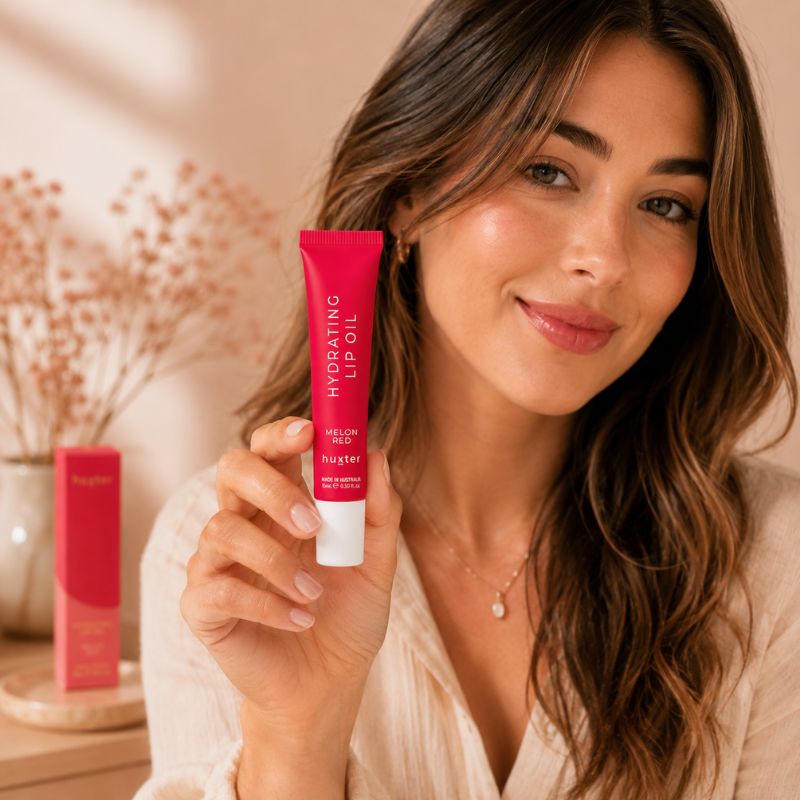 Woman holding Huxter Melon Red Hydrating Lip Oil in warm beauty lifestyle setting