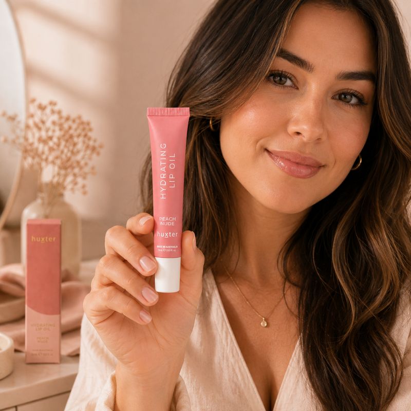Woman holding Huxter Peach Nude Hydrating Lip Oil tube in lifestyle setting