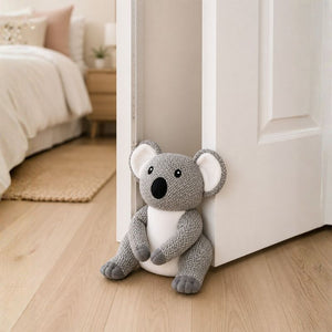 Plush toy koala door stopper sitting on a wooden floor next to a white door.