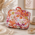 A Large hanging toiletry bag in Ivy floral print with pink and orange details with a colorful floral and abstract botanical print, featuring a pink top handle and a pink brand patch on the front, styled on a light stone surface with dried flowers and home decor props.