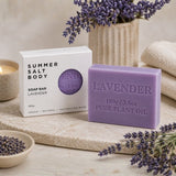 Lavender soap bar with packaging on a wooden surface with lavender flowers.
