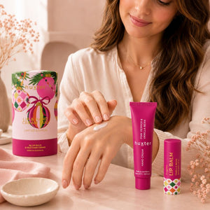 Woman applying Huxter Pink Pepper and Vanilla Bean hand cream with lip balm and Limited Edition gift box on vanity