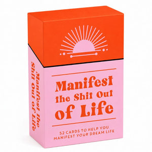 A boxed card deck titled "Manifest the Shit Out of Life" with a bright orange top panel and pink lower panel, photographed on a clean white background.