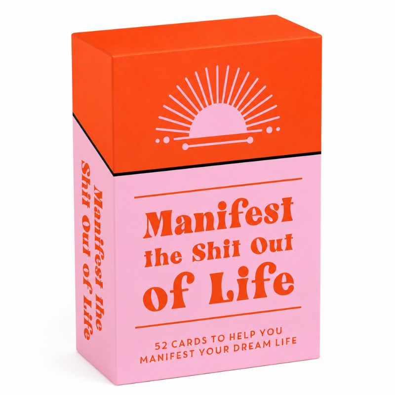 A boxed card deck titled "Manifest the Shit Out of Life" with a bright orange top panel and pink lower panel, photographed on a clean white background.