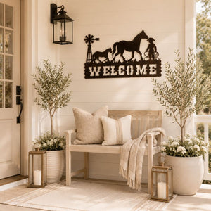 Metal horse and cowboy welcome sign displayed above a beige bench with neutral cushions and indoor olive trees in a modern entryway.