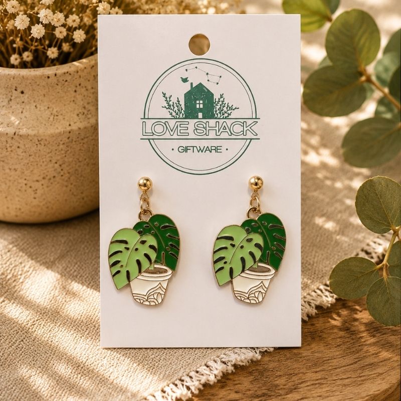 Monstera Leaf Dangle Earrings on a 'Love Shack Giftware' card with plants in the background.