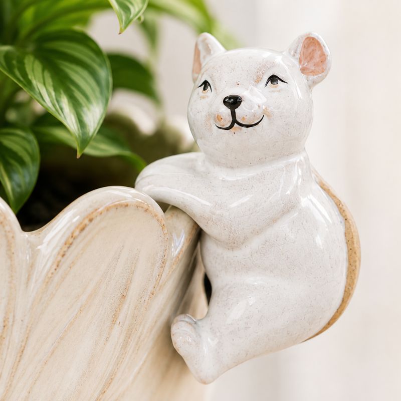 A glossy white ceramic squirrel figurine climbing a matching cream-colored planter, with green plant leaves visible in the background.-Mouse Pot Hanger White 9cm