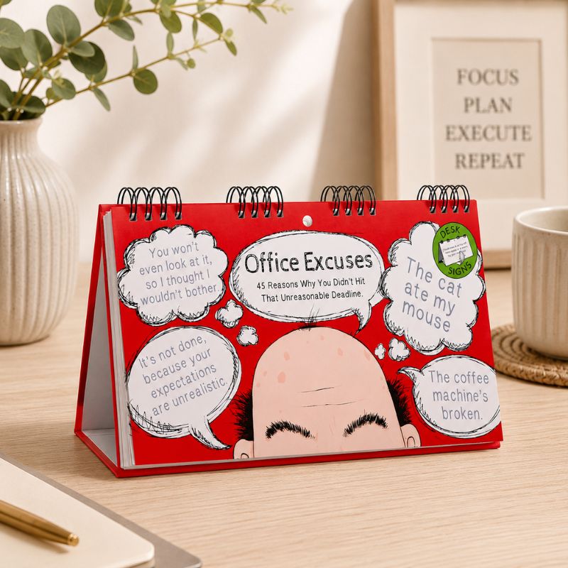 Red desk calendar titled 'Office Excuses' on a desk with a plant and mug in the background.