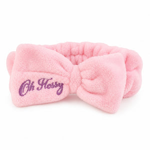 A pink plush bow headband with purple embroidered text reading 'Oh Flossy' on the left side, shown against a plain white background.
