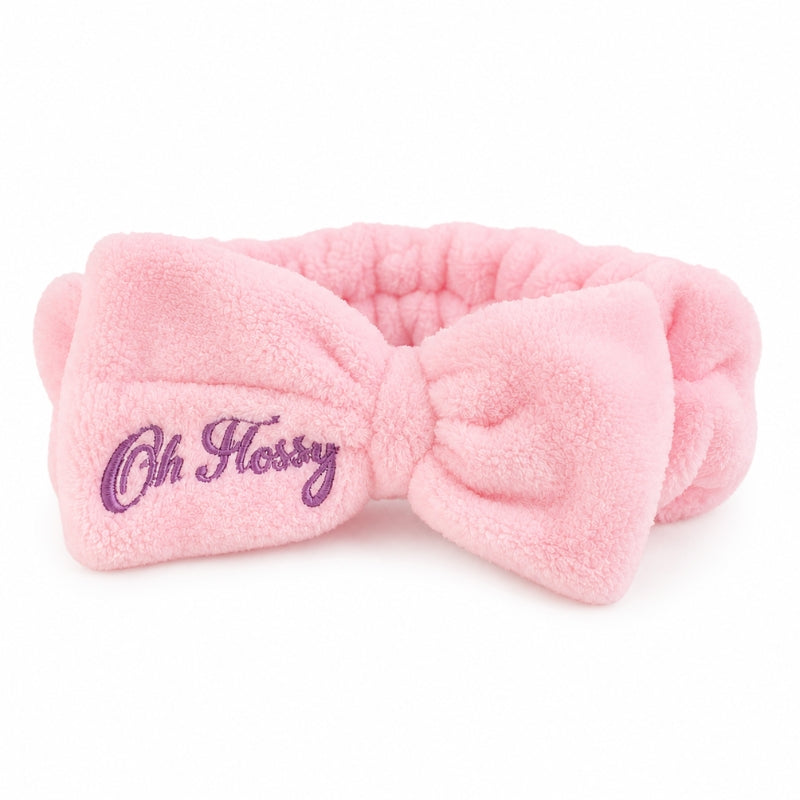 A pink plush bow headband with purple embroidered text reading 'Oh Flossy' on the left side, shown against a plain white background.