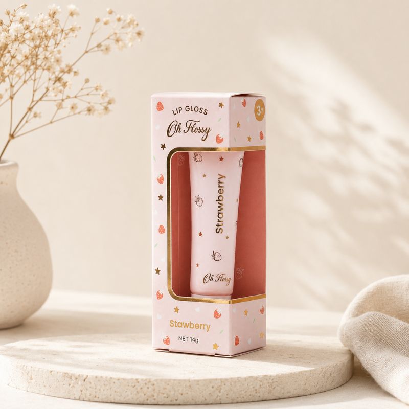 A pink lip gloss tube in a matching pink and gold box, labeled 'Oh Flossy' and 'Strawberry', displayed on a round stone tray with dried flowers and soft sunlight in the background.