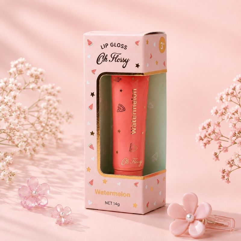 A pink lip gloss tube labeled 'Oh Hissy' and 'Watermelon' displayed inside its matching pink packaging box, styled with pink flower props on a soft pink background.