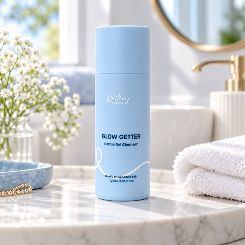 Oh Flossy Glow Getter Gentle Gel Cleanser 120ml in a pastel blue bottle on a bathroom vanity with white towels and flowers.
