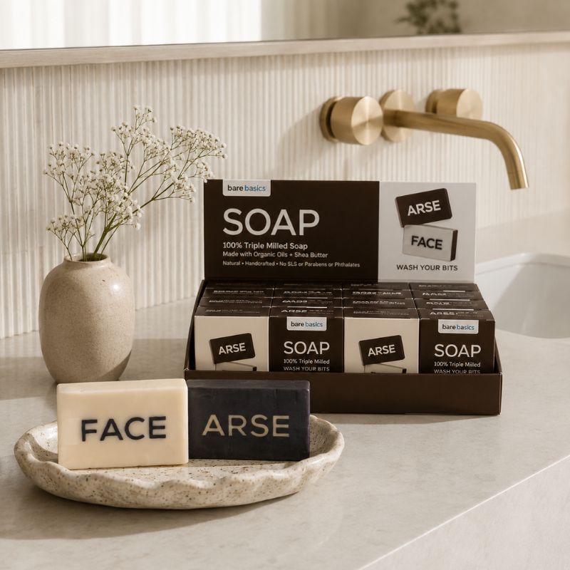 Bare Basics soap bars labeled 'Face' and 'Arse' on a bathroom counter with packaging in the background.
