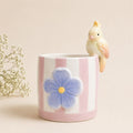 Ceramic mug with a blue flower design and a small bird figurine on a beige background