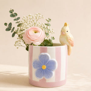 Pink ceramic vase with a blue flower design, pink rose, and small yellow bird on a beige background