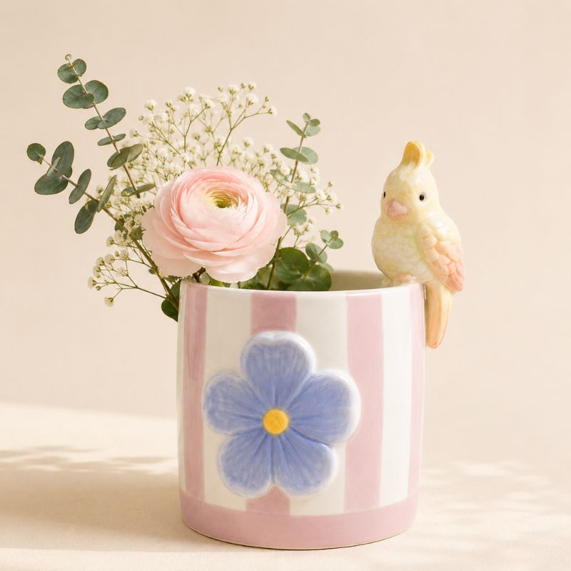 Pink ceramic vase with a blue flower design, pink rose, and small yellow bird on a beige background