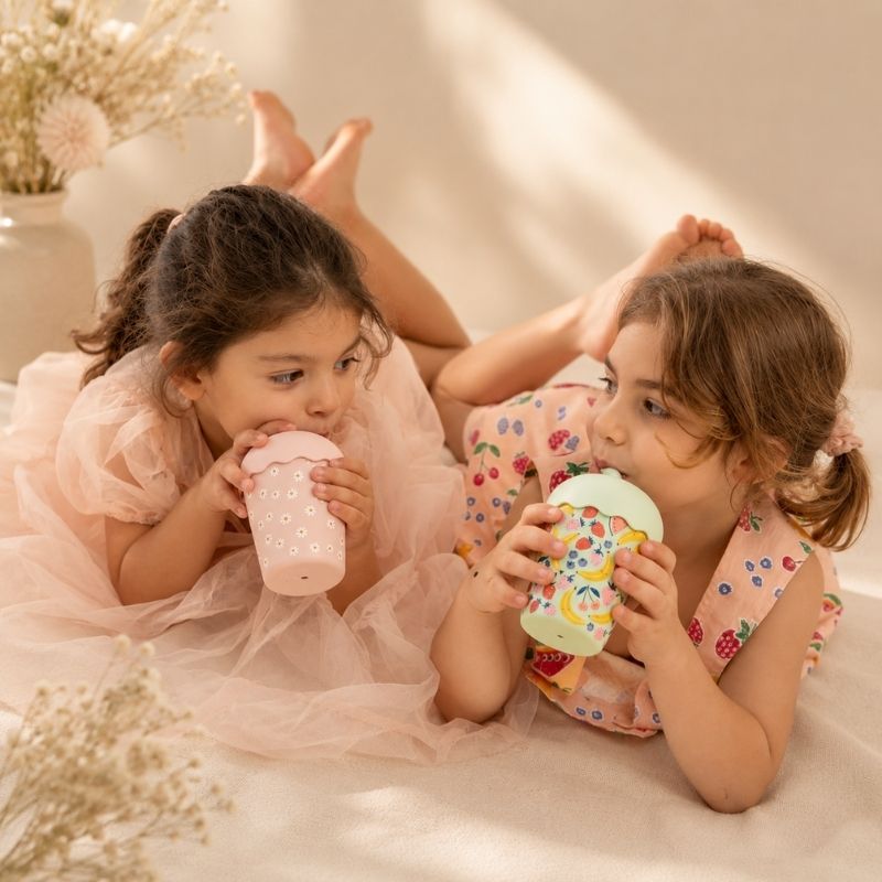 Two young girls sitting on a bed, each holding a Pink Daisy Mini Smoothie Cup & Straw 200ml