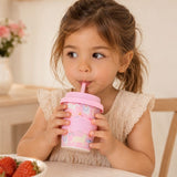 Young girl drinking from a Pink Unicorn Babychino cup (4 oz) with a straw in a cozy indoor setting.