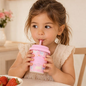 Young girl drinking from a Pink Unicorn Babychino cup (4 oz) with a straw in a cozy indoor setting.