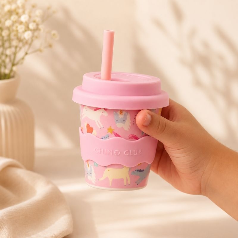 Hand holding a Pink Unicorn Babychino cup (4 oz) against a soft beige background