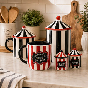 A set of ceramic kitchen canisters and a mug with a red and black striped circus-style design, displayed on a kitchen countertop with a tiled backsplash, wooden cutting board, and small plants in the background.