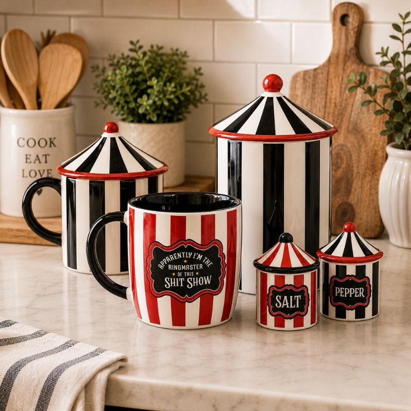 A set of ceramic kitchen canisters and a mug with a red and black striped circus-style design, displayed on a kitchen countertop with a tiled backsplash, wooden cutting board, and small plants in the background.