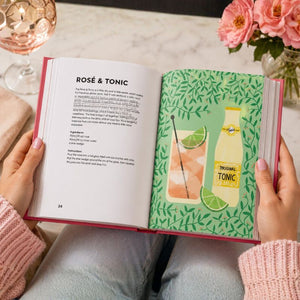 Open book with a Rosé & Tonic recipe and a lime illustration on a table with flowers and a glass.