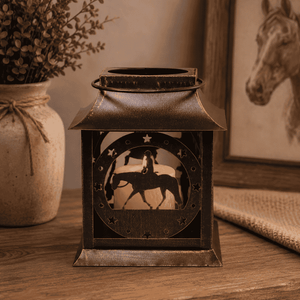 Decorative lantern with horse design on a wooden surface, next to a vase with plants and a framed picture.