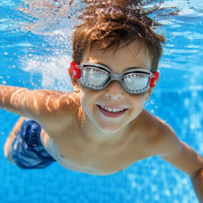 Child swimming underwater wearing Shark Grey JAWS swim goggles in a clear blue swimming pool