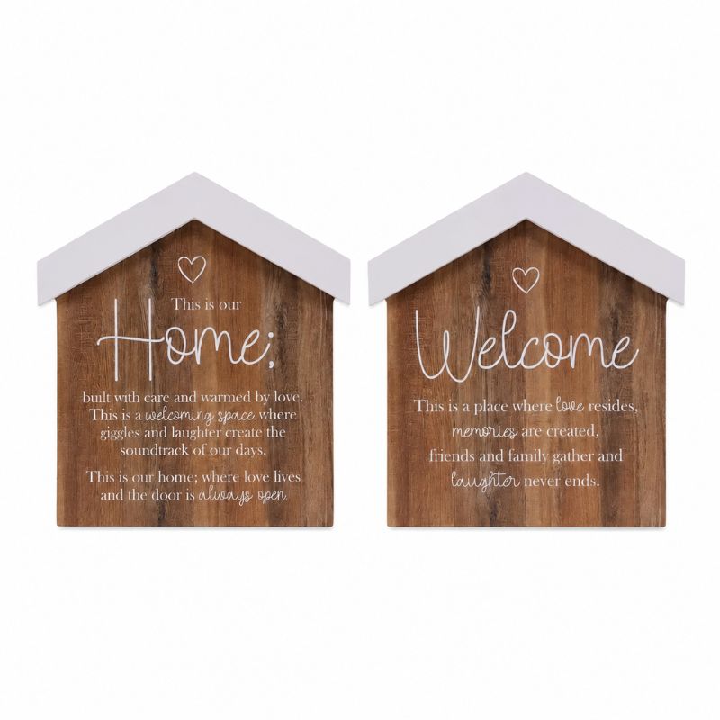 Two small house-shaped wooden wall signs with white roofs and white lettering, shown side by side on a light gray background. The left sign reads 'This is our Home' and the right sign reads 'This is our Welcome'.